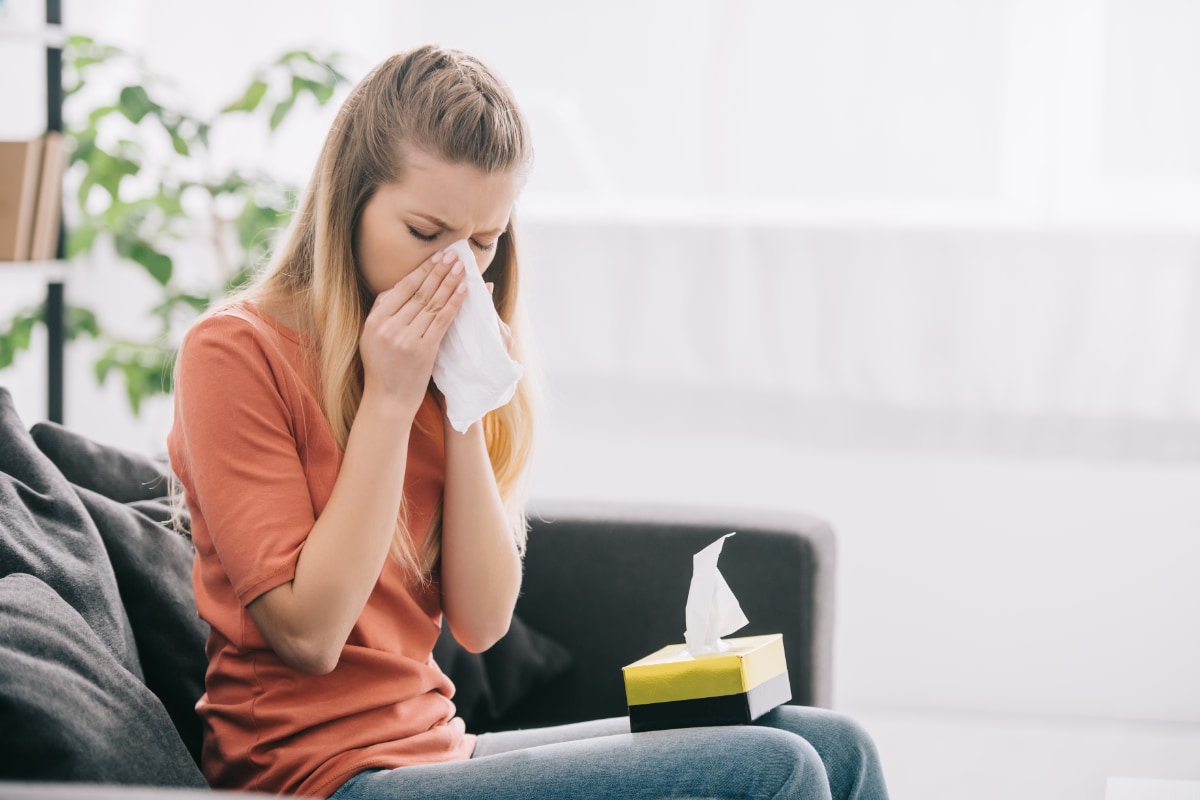 woman sitting on living room couch sneezing into a tissue