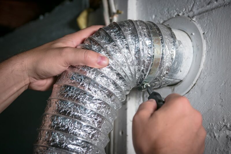 person unscrewing a dryer vent hose from the wall